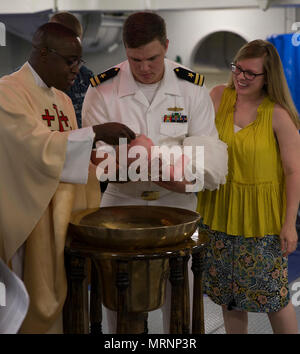 NORFOLK, Virginia (24. Juni 2017) - Lt Jamal Scarlett, von Murrieta, Kalifornien, ein Seelsorger an Bord der USS Gerald R. Ford (CVN 78), tauft, der Sohn der Leutnant John 'Jack' Curran, aus Silver Spring, Maryland, ein Ford deck Division Officer, und Leutnant Emily Curran, aus San Antonio, Texas, ein ehemaliger Ford nukleare Oberfläche warfare Officer. Der Brauch der tauft Säuglinge an Bord von Schiffen der britischen Royal Navy, in der die Kinder unter oder im Inneren des Schiffes Bell getauft ist. (U.S. Marine Foto von Mass Communication Specialist 3. Klasse Elizabeth A. Thompson) Stockfoto