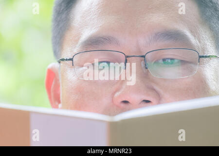 Im mittleren Alter Mann mit Brille, Menschen sitzen in der Spüle, Bücher oder Notebooks im grünen Garten, glücklich, in die Stille. Stockfoto