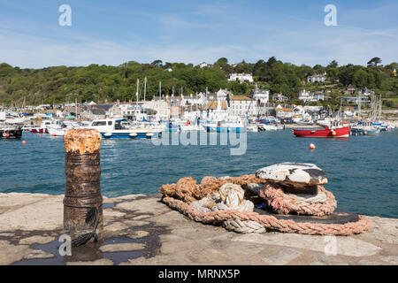 Kleine Boote vor Anker auf einem blauen Meer in Lyme Regis Hafen. Ein Bügeleisen post und Spiralkabel Seil im Vordergrund. Lichtdurchflutete Häuser sind im Hintergrund. Stockfoto