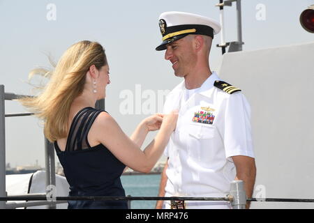 170617-N-XP 344-081 MANAMA, Bahrain (27. Juni 2017) Lt.Cmdr. Michael T. McArawas, kommandierender Offizier der Cyclone-Klasse Coastal Patrol Schiff USS Thunderbolt (PC 12) und heimisch in Erie, Pennsylvania, zweiter von, hat seinen Befehl-auf-See Pin auf seine Uniform von seinem Ehepartner, die nach einem Wechsel der Befehl Zeremonie an Bord während pierside am Naval Support Activity Bahrain statt. Thunderbolt ist einer von 10 PCs, Manama, Bahrain, deren Aufgabe es ist, Küstenwache und verbot Überwachungsanwendungen eingesetzt. (U.S. Marine Foto von Mass Communication Specialist 2. Klasse Victoria Kinney) Stockfoto