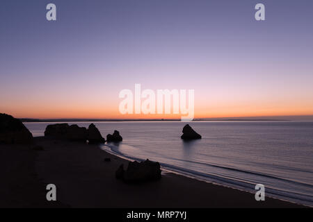 Sonnenaufgang über dem Meer in Lagos, Portugal. Leere Sandstrand mit Felsen bei Sonnenaufgang. Stockfoto