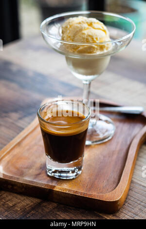 Ein Schuß Glas heißem Espresso Kaffee serviert mit Vanilleeis 'Affogato' italienisches Dessert auf hölzernen Tisch in Coffee Shop, selektive fo Stockfoto