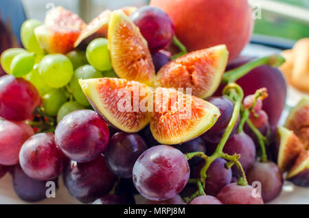 Gesundes, frisches Frühstück Obst in der Außenanlage mit weißen und Burgund Weintrauben, Feigen, Pfirsiche in sonniger Morgen auf der Terrasse. Food Lunch Sorte auf outdoo Stockfoto