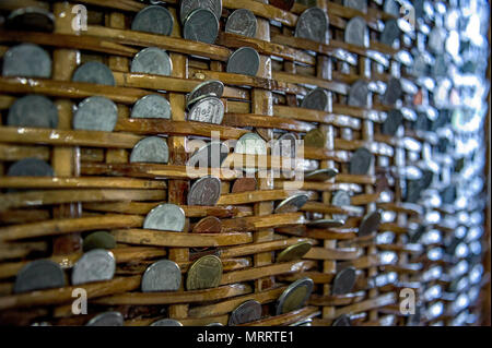 Münzen in einem Korb. Geld in einen Korb. Münzen verschiedener Typen und Werte zwischen den Geweben von Rattan Korb eingefügt. Stockfoto