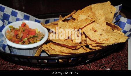 Chips in einem Korb Tablett mit nacho Dips in eine kleine Schüssel mit blau-weiss kariert Serviette Stockfoto