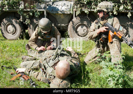 Der Soldat mit der Ukraine 1 Airmobile Bataillon, 79 Air Assault Brigade führt bekämpfen Erste Hilfe auf einem simulierten Unfall, während ein anderer Soldat Sicherheit bei einem Bataillon Feld Training am Yavoriv Combat Training Center auf dem internationalen Friedens und der Sicherheit, in der Nähe der Yavoriv, Ukraine, zieht am 30. Juni. Yavoriv CTC Personal, zusammen mit Mentoren aus 45Th der US Army Infantry Brigade Combat Team, führte die Ausbildung von Soldaten aus dem 1 Mrd., 79. regt., bei der die Drehung des Bataillon durch die YAVORIV CTC. Der 45. ist in der Ukraine als Teil des Gemeinsamen bereitgestellt Stockfoto