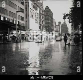 1960, historische Ansicht eines nassen, feuchten, ziemlich spärlich Leicester Square, London, England, zeigt das Empire Theater, ursprünglich im Jahr 1884 für verschiedene Theater gebaut und dann wieder in den 1920er Jahren für das Zeigen von Spielfilmen. In Mecca Bingo 1961 übernahm das Imperium und verwandelte es in einem MGM Kino und ein Mekka Dance Hall. In dieser ära Verkehr könnte gehen hinter dem Empire, etwas, das nicht geschehen. Stockfoto