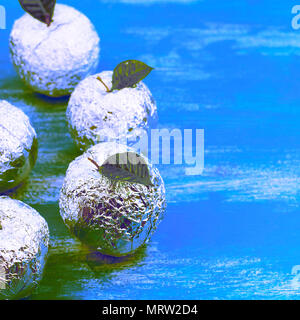 Fünf Äpfel in der shell Folie mit natürlichen, grünen Blätter Surrealismus. Holz- candy blauen Hintergrund. Flach Top View Stockfoto