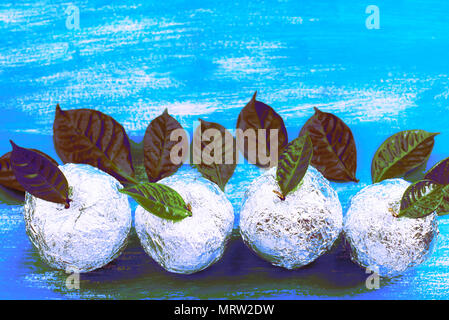 Surrealismus vier Äpfel in Folie eingewickelt sind natürliche grüne Blätter. Holz- candy blauen Hintergrund. Flach Top View Stockfoto