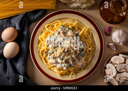 Flach mit gekochten Spaghetti mit cremiger Sauce und Käse unter frischen Zutaten zum Kochen angeordnet Stockfoto