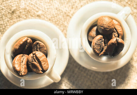 Kaffeebohnen in einer schönen kleinen Porzellan Tassen close-up. Starker Kaffee Poster. Stockfoto