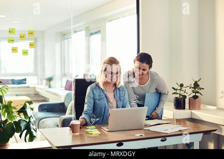 Zwei lächelnde junge Unternehmerinnen zusammen an einem Schreibtisch in einem Büro Schreibarbeit Diskutieren und Arbeiten mit einem Laptop Stockfoto