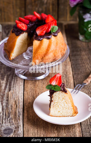 Hausgemachte bundt Cake mit dunkler Schokolade ganache Glasur und frische Erdbeeren auf der Oberseite auf rustikalen Holztisch Stockfoto