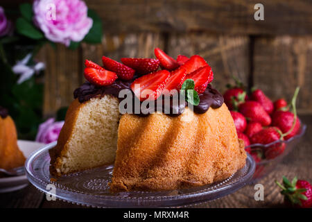 Hausgemachte bundt Cake mit dunkler Schokolade ganache Glasur und frische Erdbeeren auf der Oberseite auf rustikalen Holztisch Stockfoto