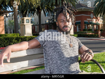 Hübscher junger afrikanischer amerikanischer Mann sitzt auf der Bank im Park. Stockfoto