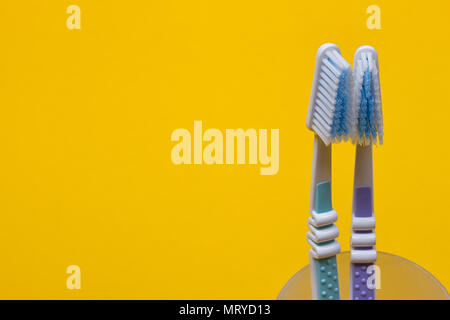 Zwei Zahnbürsten in einem Glas auf den gelben Hintergrund. Ansicht von oben Stockfoto