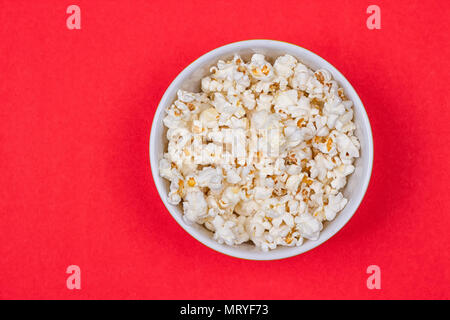 Schüssel mit lecker Popcorn verschüttet auf rotem Hintergrund Stockfoto