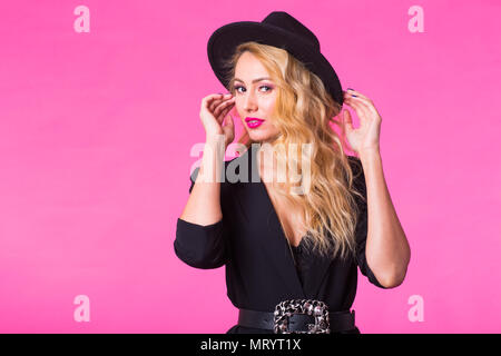 Wunderschöne junge blonde Frau in Schwarz Eleganter modischer Hut auf rosa Hintergrund posiert. Stockfoto