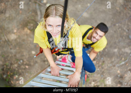 Junge Frau im Kletterpark Seilschaft auf der Leiter beim Teambuilding workshop Stockfoto