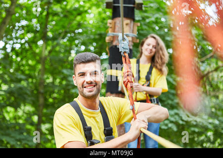 Junger Mann im Hochseilgarten mit Seil gesichert ist stolz auf seine Leistung Stockfoto