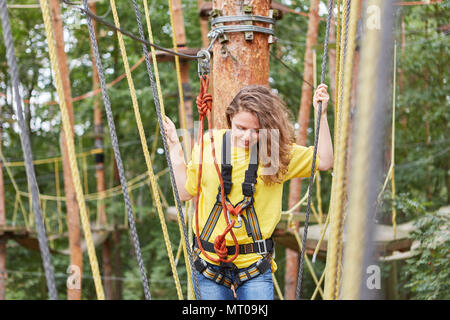 Junge Frau ist ausgleichend auf einer Brücke in den kletterwald als Teambuilding Aktivität Stockfoto