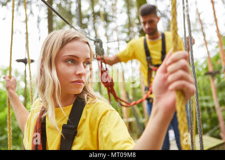 Ängstliche junge Frau kämpft mit Vertigo auf einer Brücke in den Hochseilgarten Stockfoto