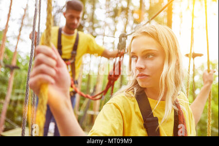 Junge Frau lernt, klettern im Hochseilgarten oder klettern Wald im Sommer Stockfoto