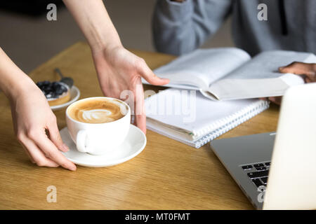 Kellnerin serviert Cappuccino zu Cafeteria Besucher im Cafe Tabelle, Stockfoto