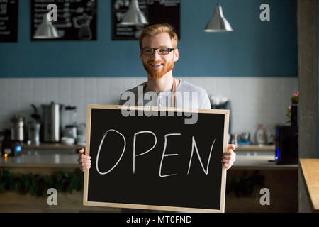 Rothaarige lächelnd Mann mit offenen Zeichen lädt zu neuen Café Stockfoto