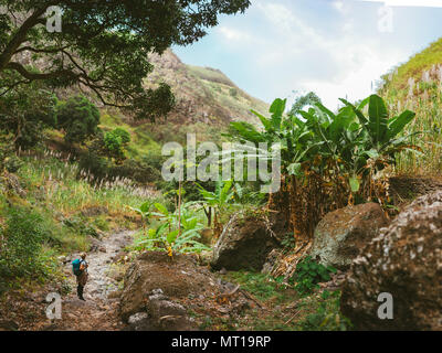 Weibliche Wanderer einen Rest in wunderbaren üppigen Canyon voller exotischer Vegetation. Viele tropischen Obstbäumen, Zuckerrohr wachsen oben auf die Berghänge auf der Insel Santo Antao Kap Verde Stockfoto