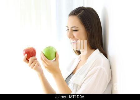 Smiley girl Holding zwei rote und grüne Äpfel auf einer Wand zu Hause Schiefe Stockfoto