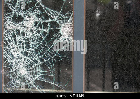 Nahaufnahme eines zersplitterten Glasfensters mit mehreren Aufprallstellen und Spinnennetzrissen, die Vandalismus oder versehentliche Sachschäden hervorheben Stockfoto