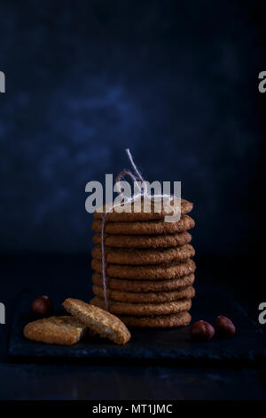 Gesunde hausgemachte oatmeal Cookies mit Haselnüssen über dunklen rustikalen Hintergrund, Low Key Stockfoto