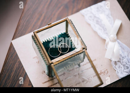 Wunderschöne goldene Hochzeit Ringe in einem vintage Glas, auf der Hochzeit Einladung und Holztisch Hintergrund Stockfoto