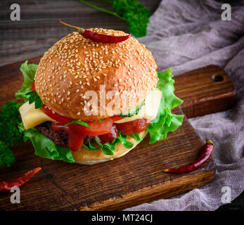 Hamburger mit Rindfleisch, Käse und Gemüse auf rustikalen braunen Tisch, Nahaufnahme Stockfoto