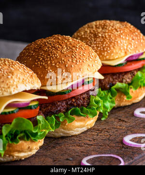 Hamburger mit Rindfleisch, Käse und Gemüse auf rustikalen braunen Tisch, Nahaufnahme Stockfoto