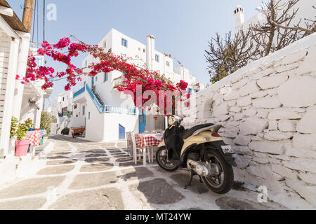 MYKONOS, Griechenland - Mai 2018: die alten gepflasterten Straße in Mykonos Stadt Stadtteil Little Venice, Restaurant und Bush in der Blüte. Retro scooter im Vordergrund Stockfoto