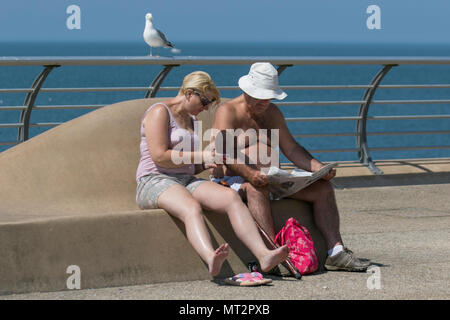 Sitzende paar Zeitung lesen in der Sonne in Blackpool, Lancashire. UK Wetter. 28 Mai, 2018. Hellen sonnigen Start in den Tag an der Küste wie Urlaubern und Touristen Annehmlichkeiten und Attraktionen an der Strandpromenade im warmen Sonnenschein. Credit: MediaWorldImages/AlamyLiveNews Stockfoto