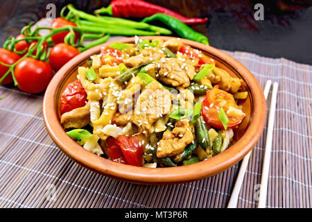 Thai Nudeln Wok mit Hähnchenfleisch, Tomaten, Sojasauce und grüne Bohnen mit Sesam bestreut Samen in einer Platte auf einem Bambus Serviette auf dem Hintergrund einer Stockfoto