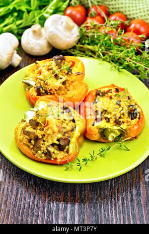 Paprika süss, gefüllt mit Pilzen, Tomaten, Couscous und Käse in einem grünen Schild auf Küchenpapier, Gabel, Petersilie vor dem Hintergrund der Dunklen nicht Stockfoto