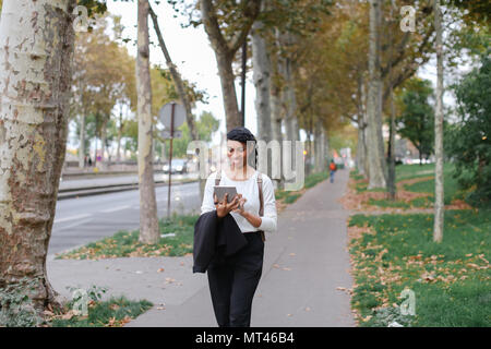 Schöne schwarze Mädchen zu Fuß nach Klassen mit Tablet auf der Straße mit Laub. Stockfoto