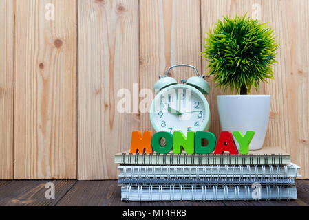 Montag Buchstaben text und Notebook Papier, Wecker und wenig Deko Baum in weiße Vase auf hölzernen Hintergrund, hallo Montag Konzept Idee. Stockfoto