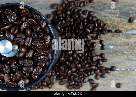 Fokus auf gerösteten Kaffeebohnen in einer kaffeemühle von Hand. Und geröstete Kaffeebohnen auf Holz- Hintergrund. Stockfoto