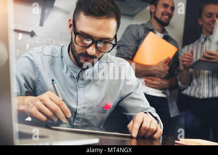 Bärtige Gläser Manager analysiert das Ergebnis der Aktien auf Tablet Bildschirm. Architekt zeichnet Projekt mit dem Stift auf dem Bildschirm des modernen Tablet. Konzept coworkin Stockfoto