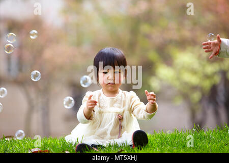 Schöne kleine asiatische Mädchen sitzen auf Rasen im Freien Stockfoto