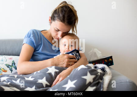 Junge Mutter, ihren kranken Kleinkind Baby in ihren Armen halten, sitzen auf einer Couch im Wohnzimmer zu Hause Stockfoto