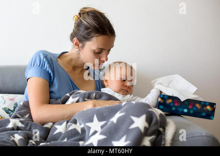 Junge Mutter, ihren kranken Kleinkind Baby in ihren Armen halten, sitzen auf einer Couch im Wohnzimmer zu Hause Stockfoto