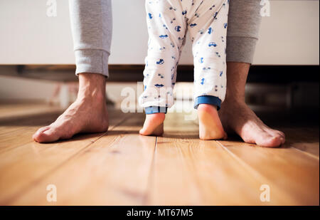 Beine von Vater und ein Kleinkind junge stehend auf dem Boden im Schlafzimmer zu Hause. Stockfoto