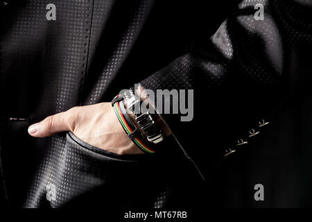 Mann im schwarzen Kostüm und mit farbigen Armbänder zur Hand. Nahaufnahme der Mann mit Schmuck auf der Hand. Stockfoto