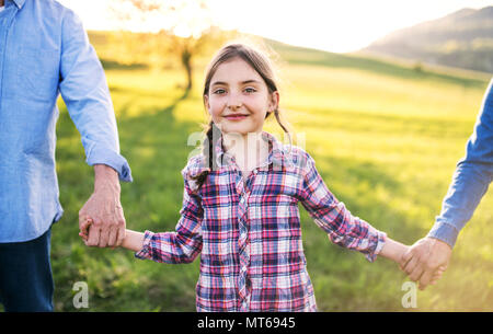 Ein kleines Mädchen mit ihrem älteren Großeltern außerhalb Wandern in der Natur bei Sonnenuntergang. Stockfoto